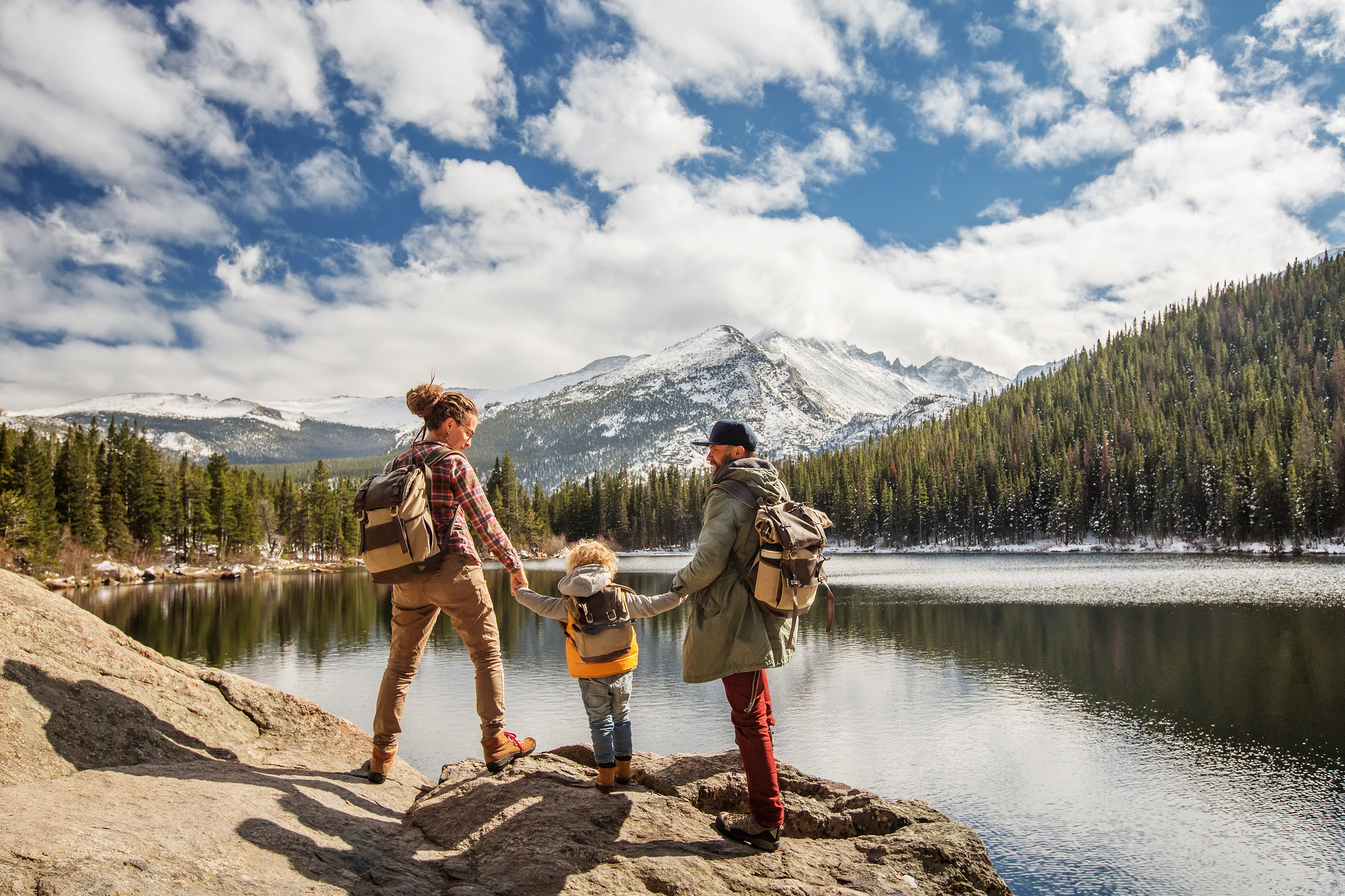 A family stands on a lakeside rock looking out at mountains