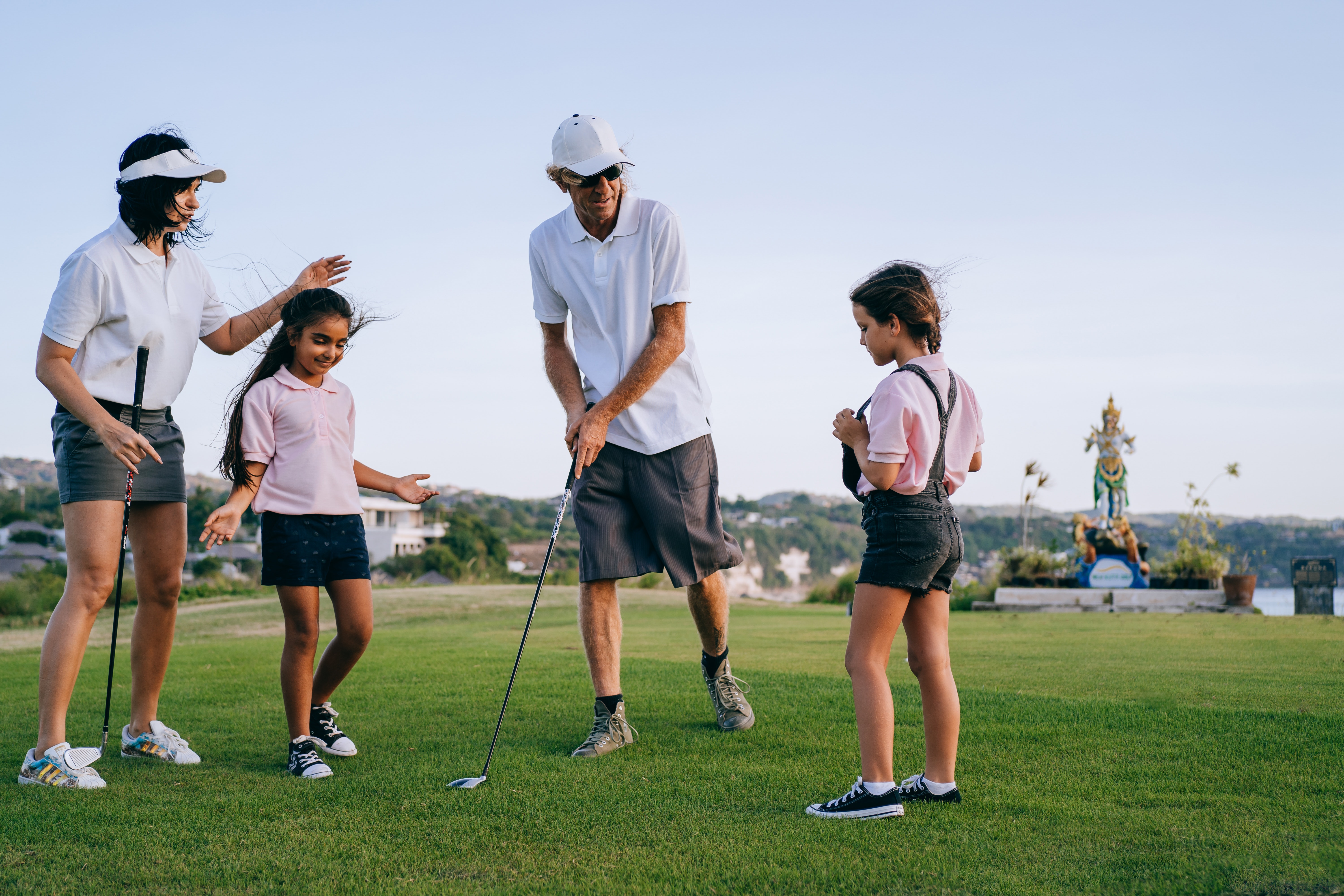 A family of four stands on a golf green on a sunny day